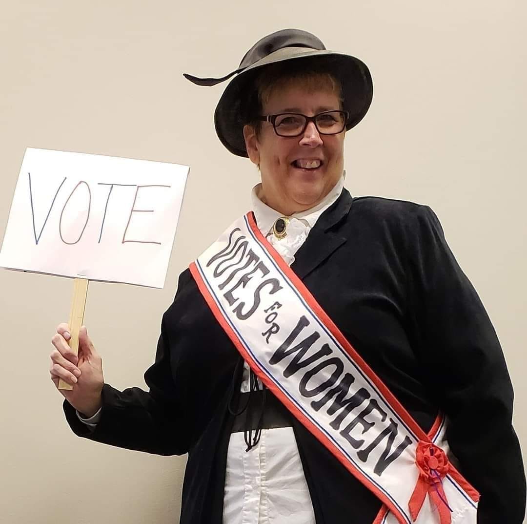 A woman wearing a suffragette costume, with a votes for women sash.